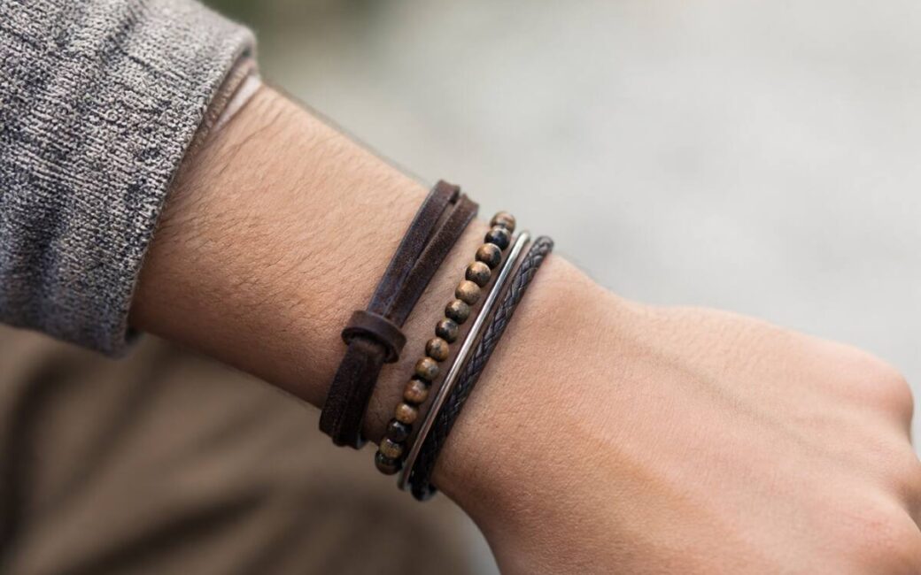 Close-up van armbanden om een pols met verschillende materialen, bij daglicht gefotografeerd.